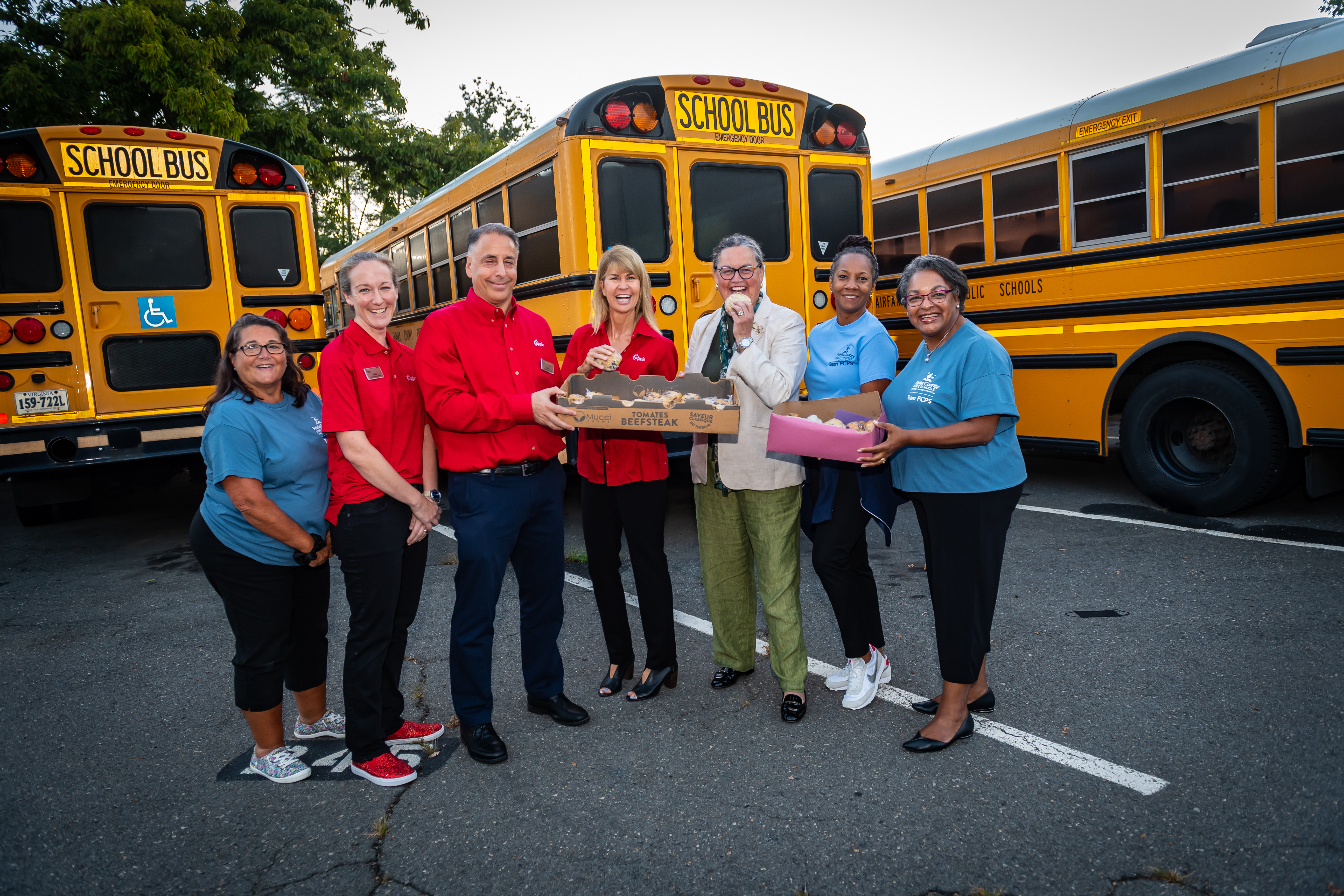 Dr. Reid and FCPS staff smile in front of a school bus. 