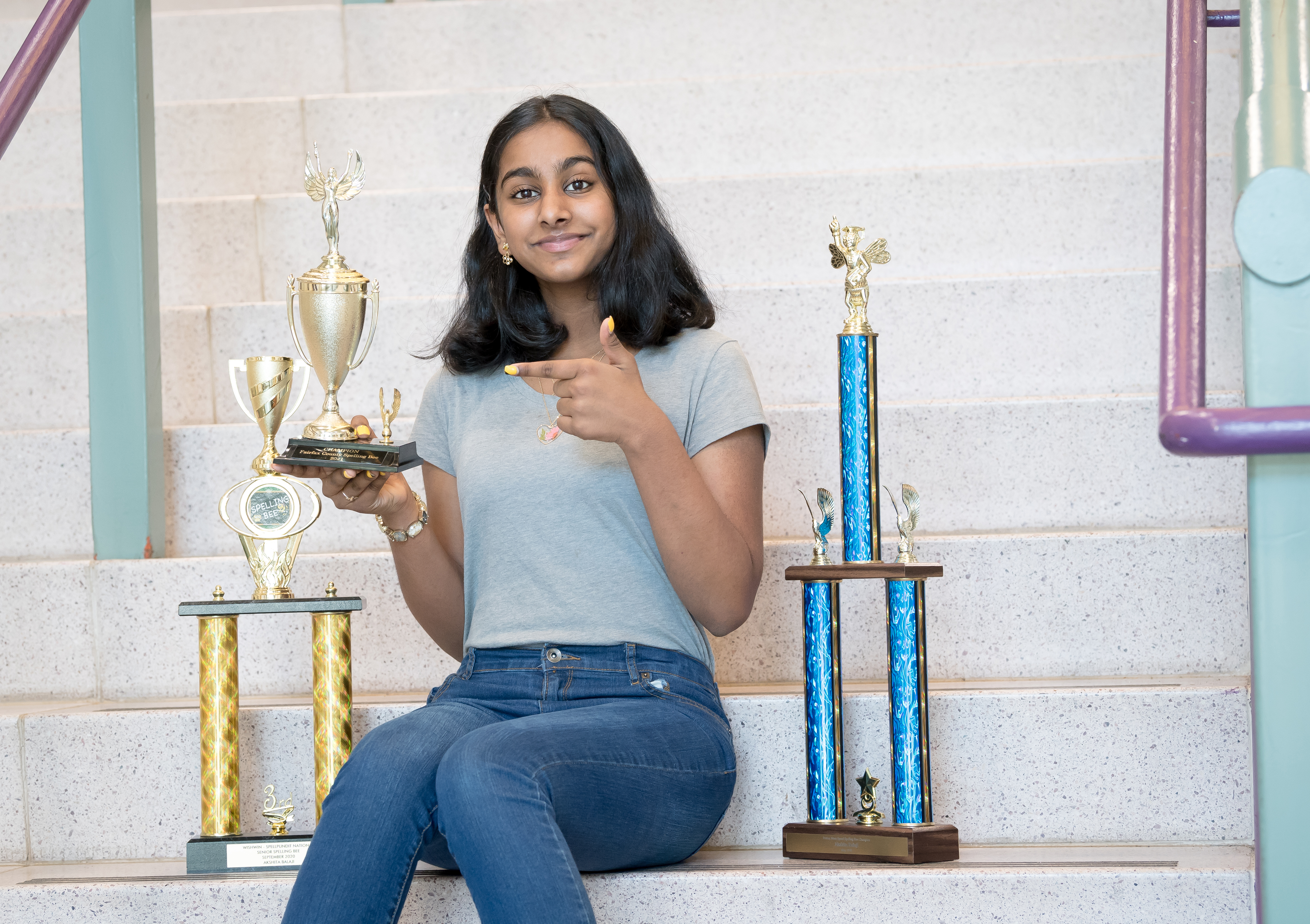 Akshita sits on stairs with a collection of spelling bee awards
