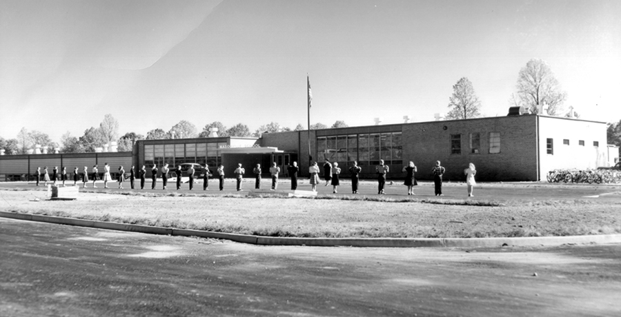 Black and white photograph of the front exterior of Masonville Elementary School. A group of students are in front of the building.