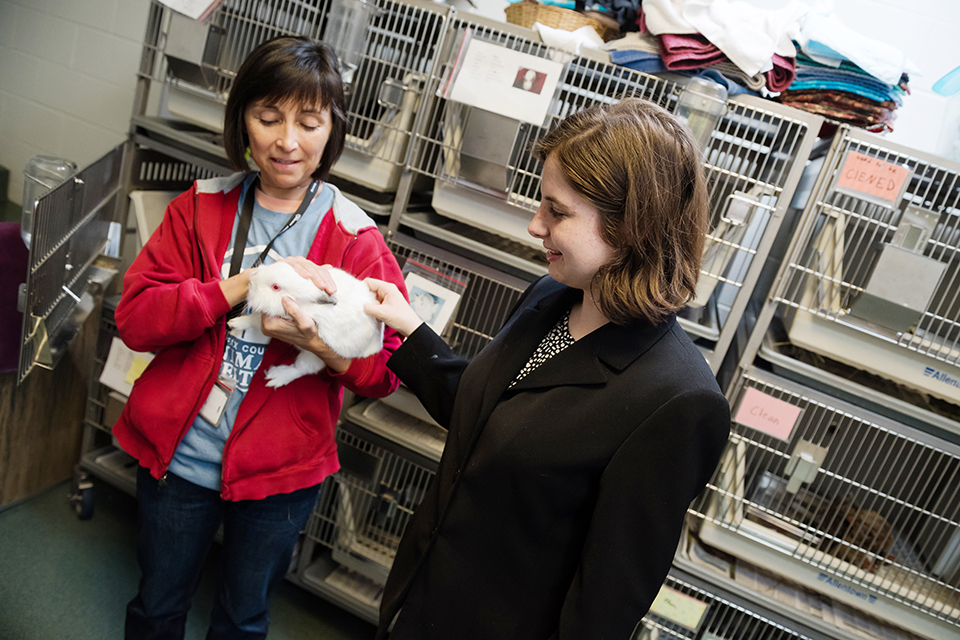 adult female holding a white rabbit with a female student petting the rabbit