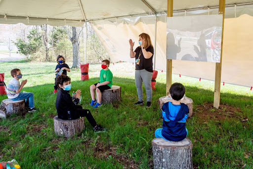 students and teacher in a tent sitting on tree stumps