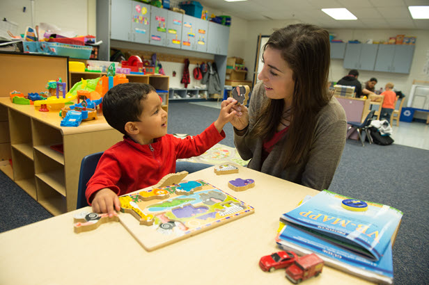 young child playing with a puzzle and high fiving his teacher