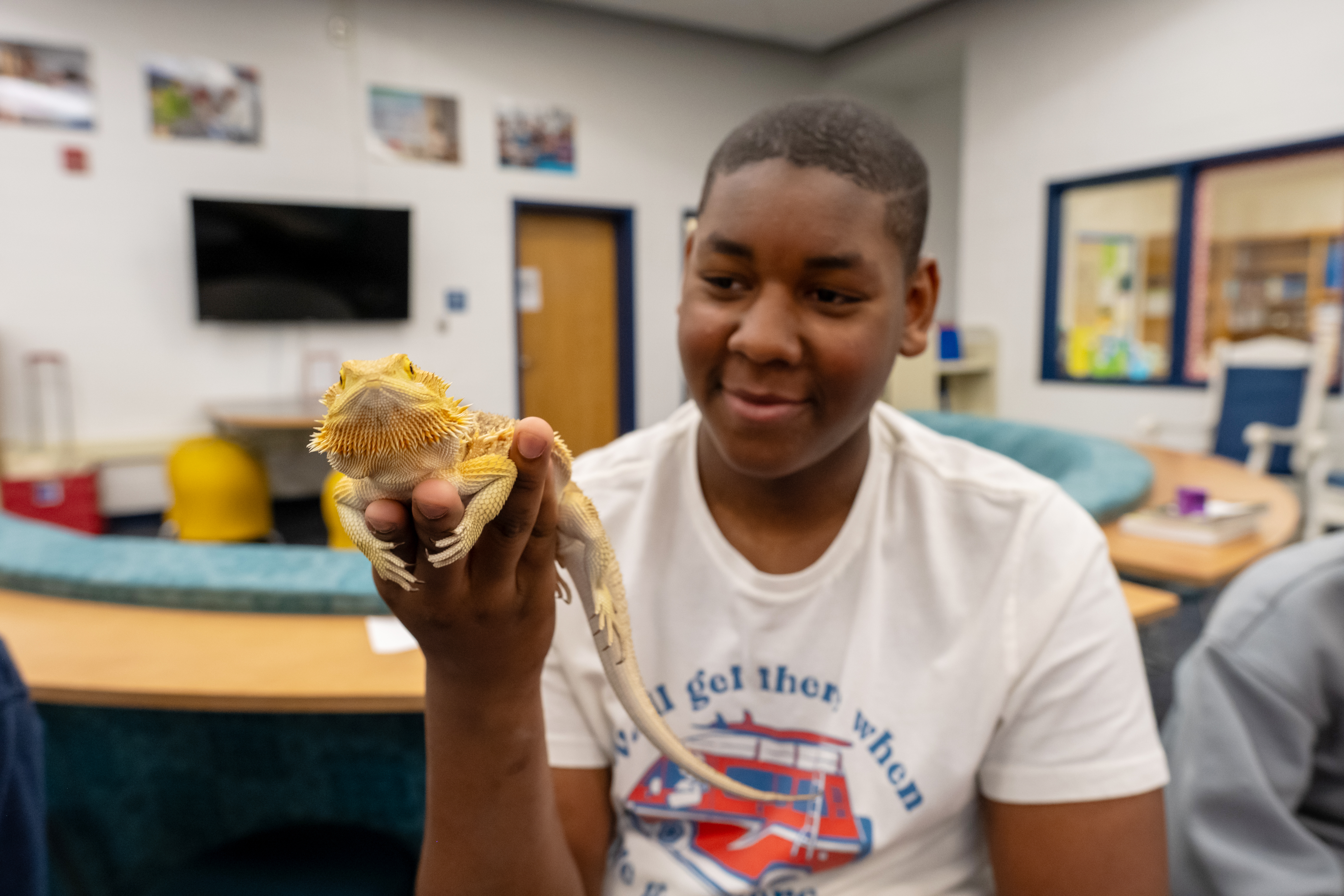 a middle school student smiles while holding up a bearded dragon