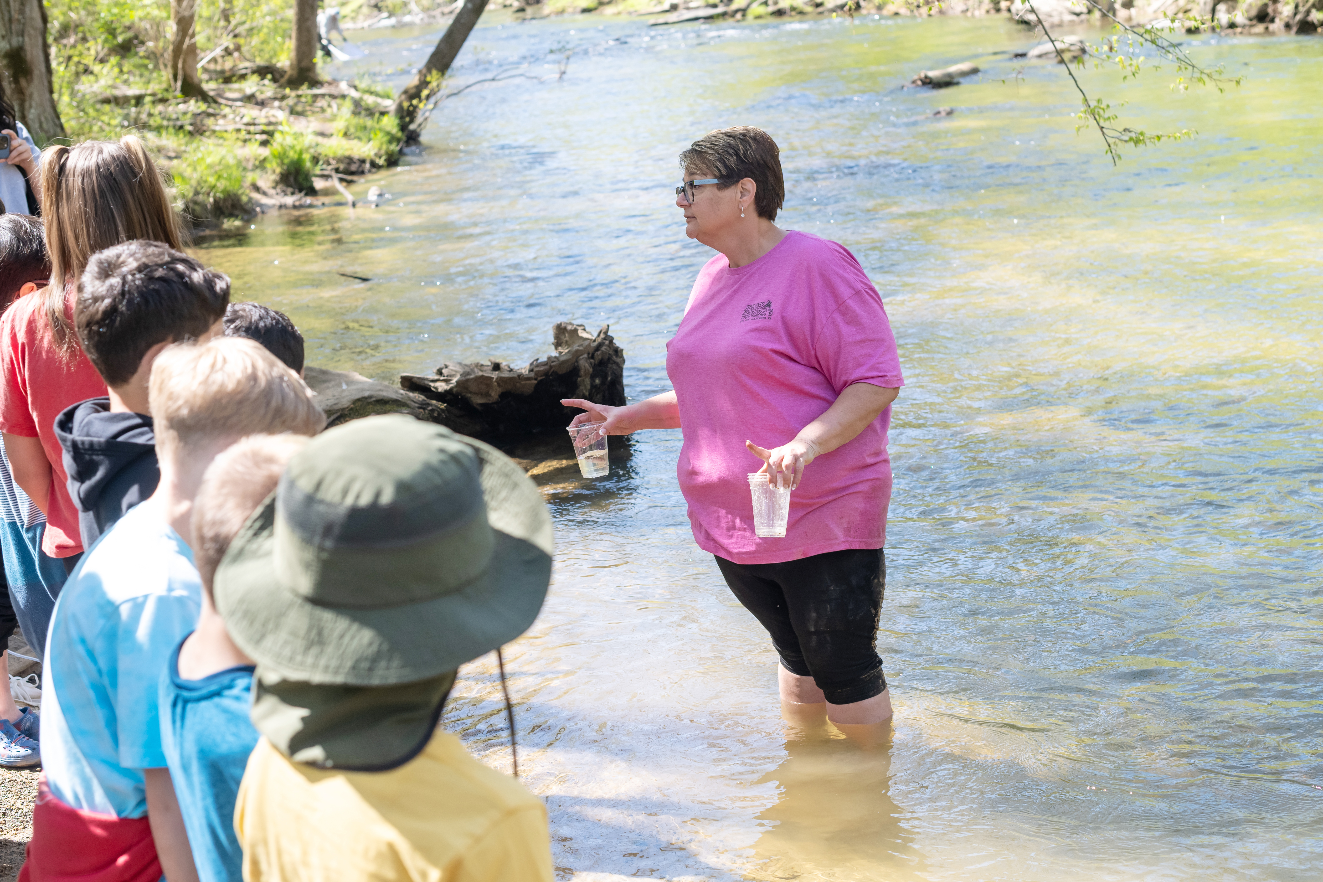 Centreville Elementary STEAM lead, MaryAnn Settlemyre, instructs students on how to release trout. She holds a cup with a single fry. Students need to hold the cup in the stream for a couple of minutes to help acclimate the young trout to the water. 