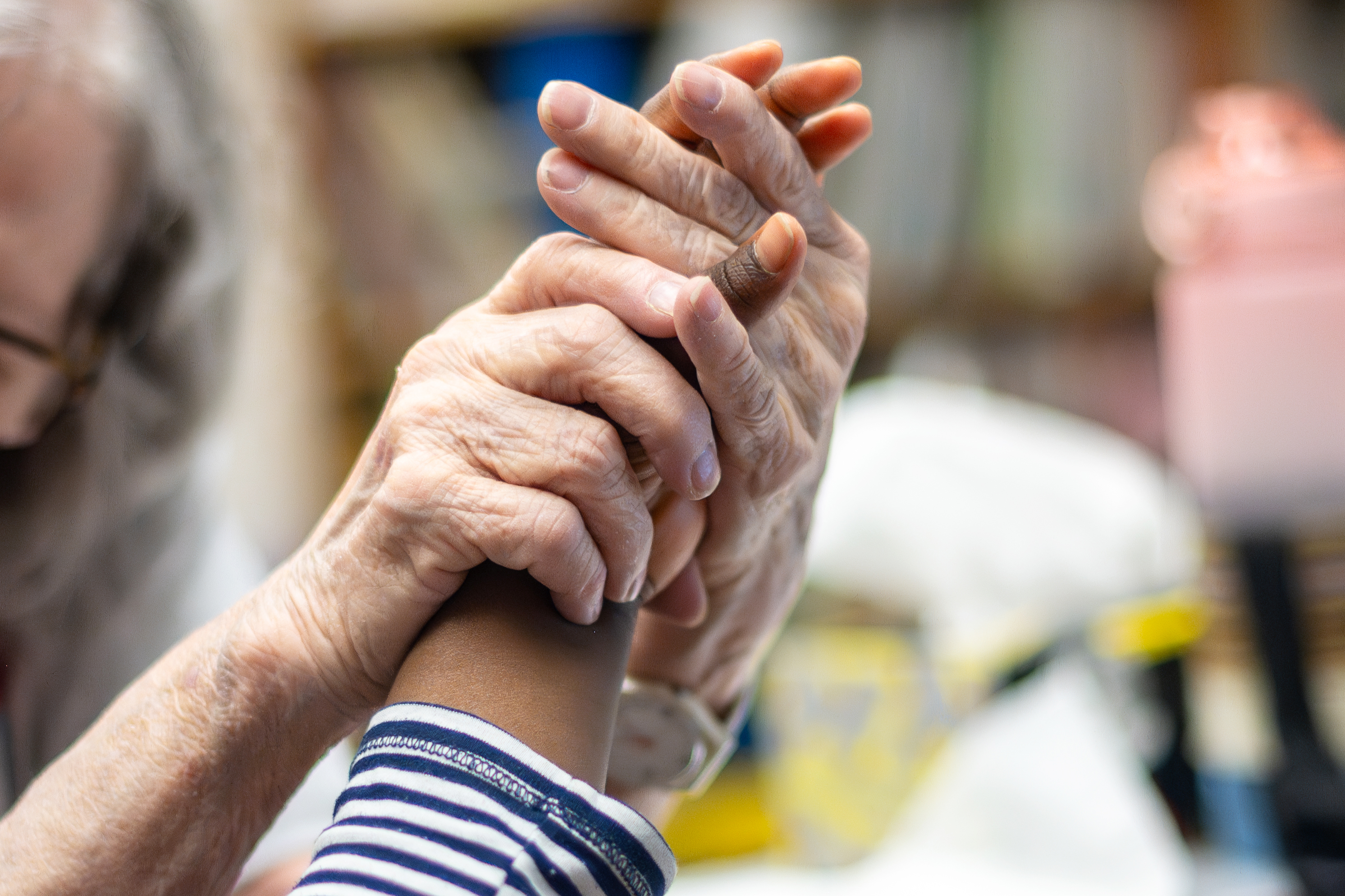 two hands of an older person grasp the hand of a young person