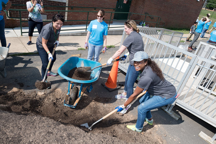 a group of teenagers digging dirt into a wheelbarrow