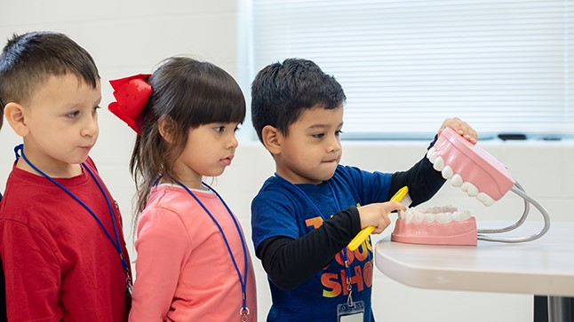 three students looking at a tooth brushing example