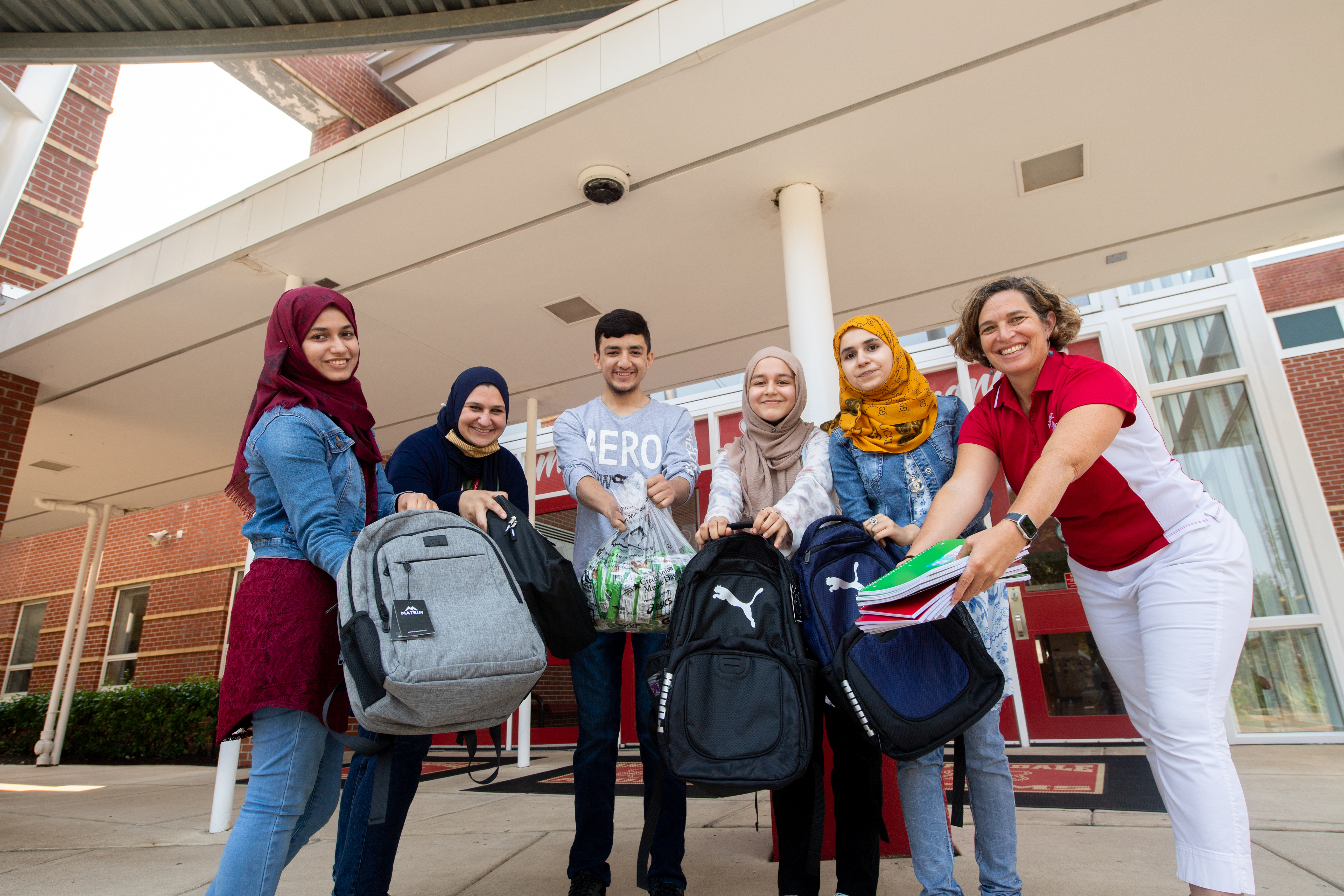 Annandale High Assistant Principal Sarah Eqab, English for Speakers of Other Languages Department Chairwoman Meredith Hedrick, and AHS students who came to the U.S. from Afghanistan over the past six years show backpacks and other supplies they've gathered to donate to newly arrived Afghan refugee students.