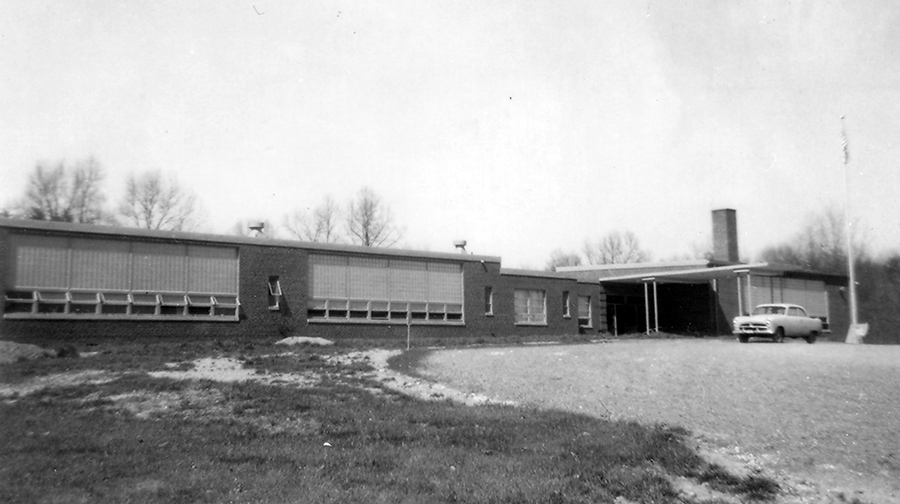 Photograph of the front exterior of Clifton Elementary School taken in 1954. A car is parked in front of the building.