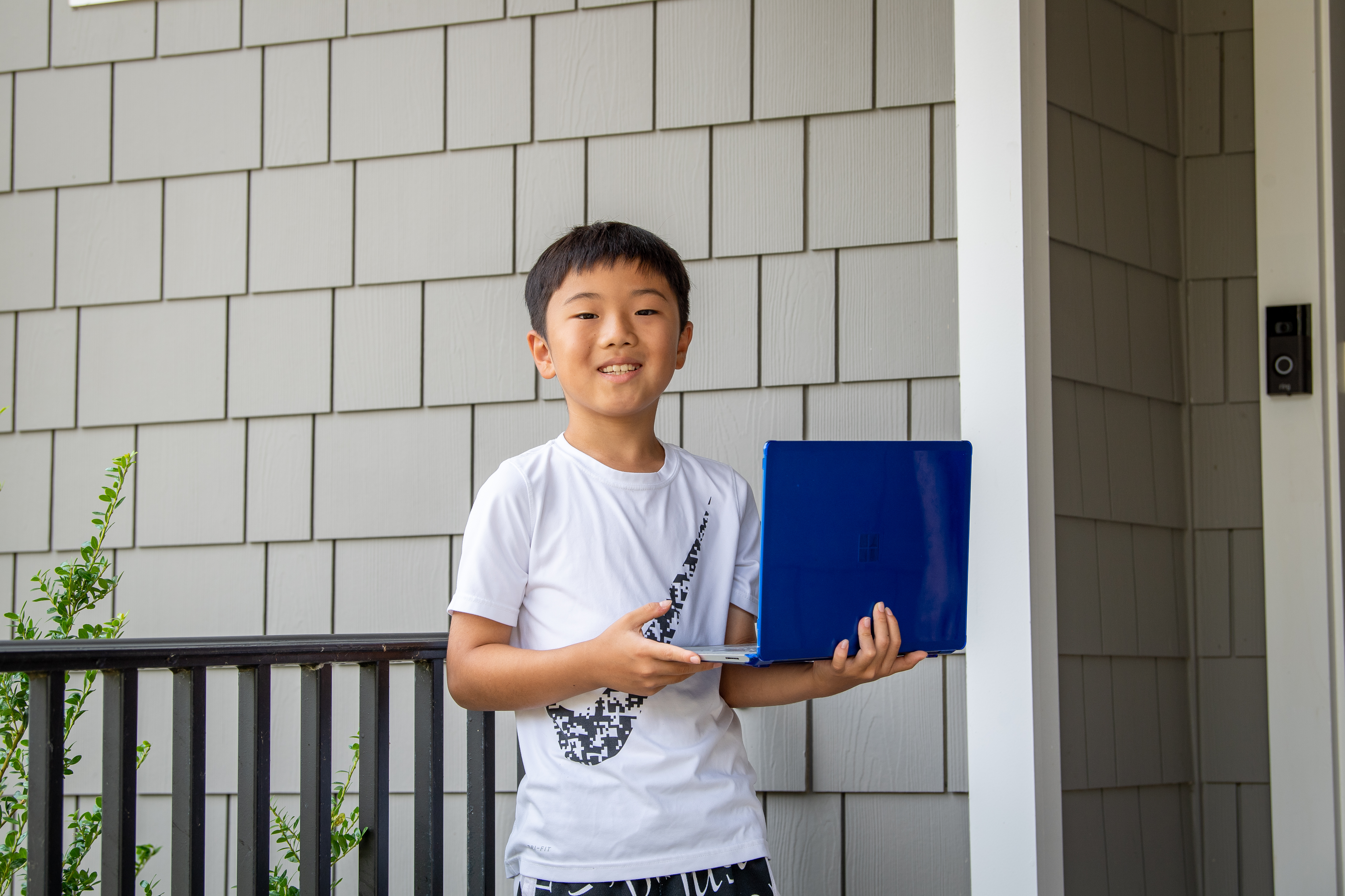 Ethan Zhang, age 9 and a Time for Kids student journalist winner, stands in front of his home with laptop in hand.