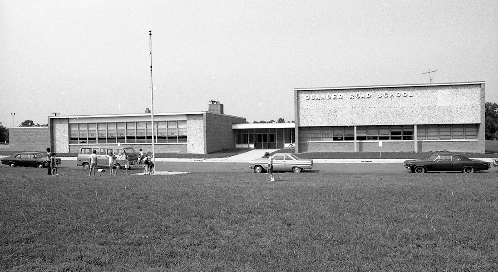 Photograph of the main entrance of Quander Road Elementary School. A small group of children is playing near the flagpole.