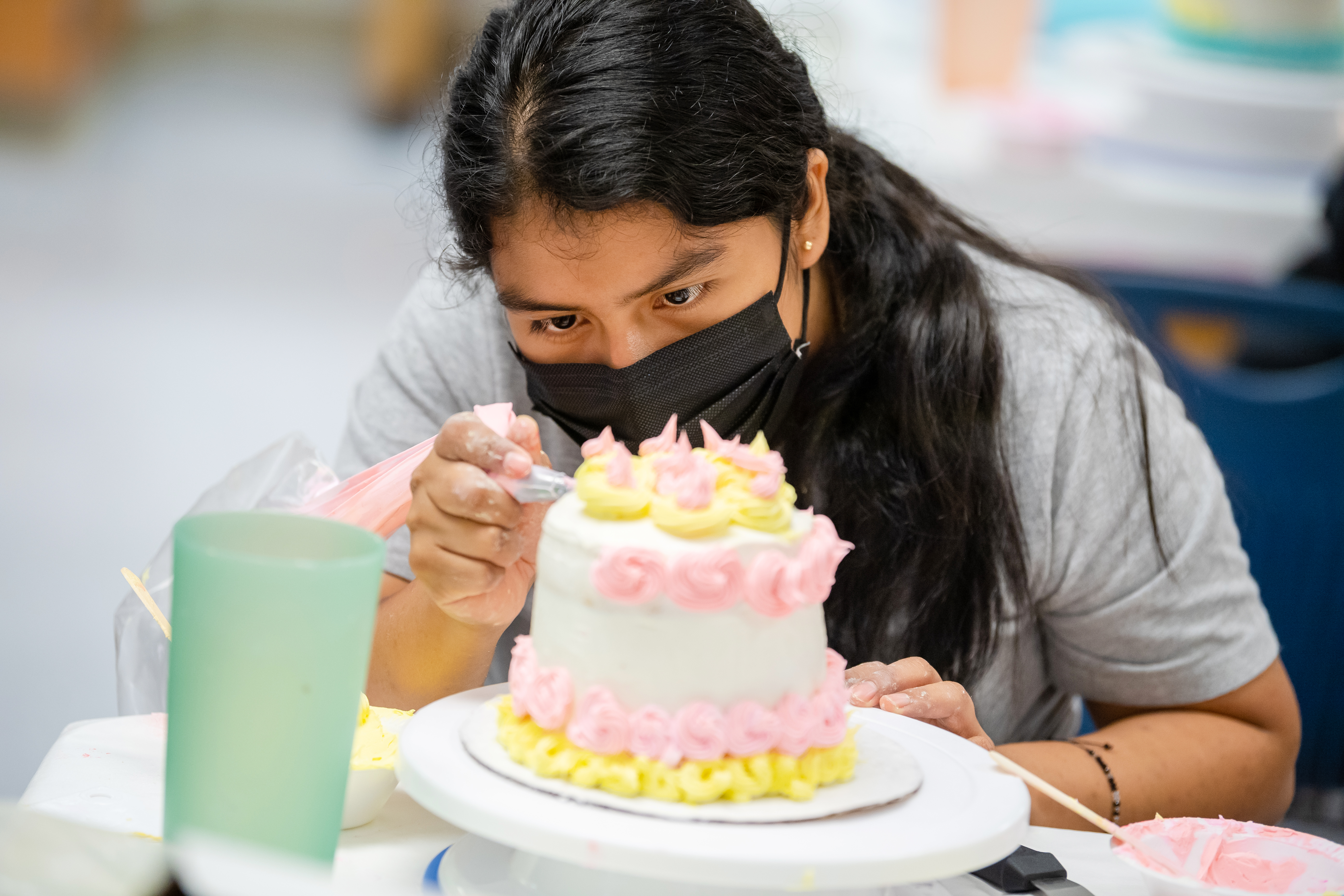 A "Modern Buttercream Techniques" student practices putting roses on a cake.