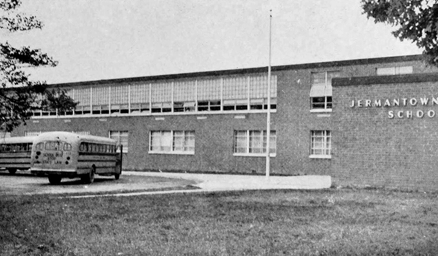 Black and white photograph of the front exterior of Jermantown Elementary School. School buses are parked in front of the building.