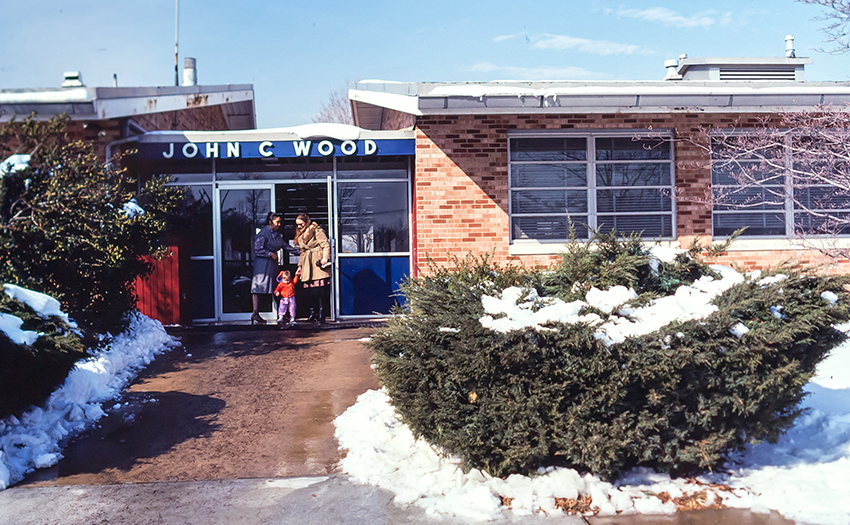 Color photograph of the main entrance of John C. Wood Elementary School. A mother and child are exiting the building.