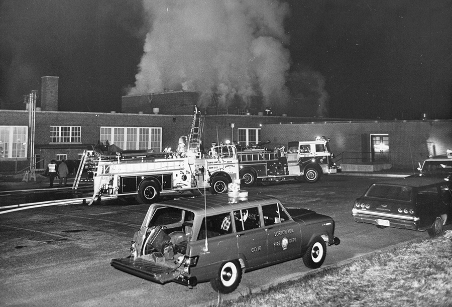 Photograph of Lorton Elementary School on the night of April 6, 1970. Fire department vehicles are parked next to the building and a large plume of smoke is issuing out of the school’s cafeteria.