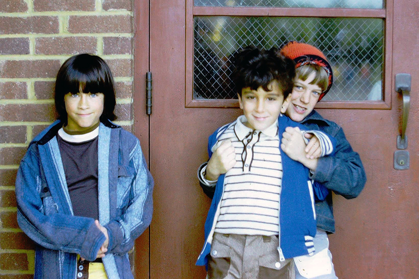 Photograph of three students standing outside Layton Hall Elementary School next to a door.