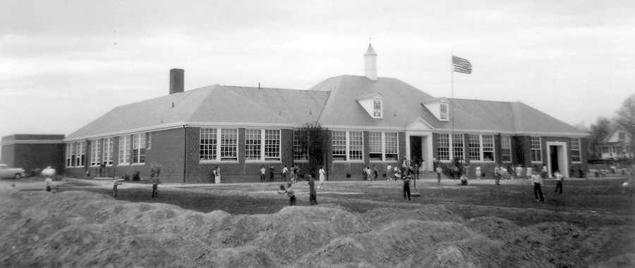 Black and white photograph of the front exterior of Lincolnia Elementary School. Children are playing on the lawn in front of the school.