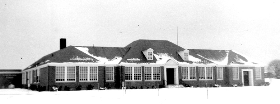 Black and white photograph of the front exterior of Lincolnia Elementary School. There is snow on the ground and on the roof of the building.