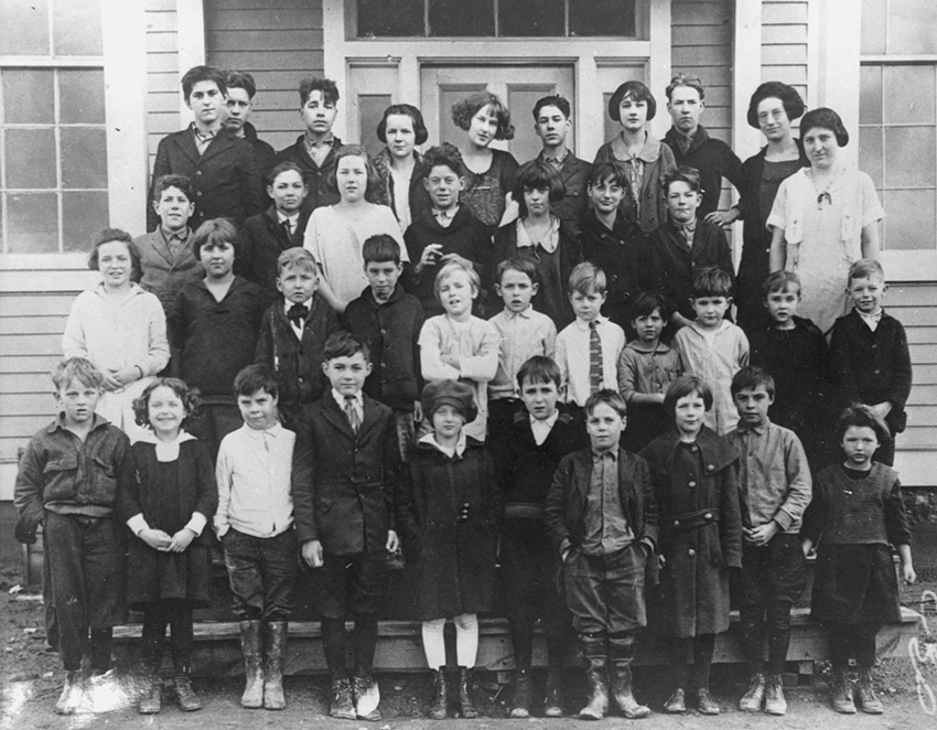 Black and white class photograph from the Lorton School. A group of approximately 35 students between the ages of 6 and 16 are standing on the steps in front of the building.