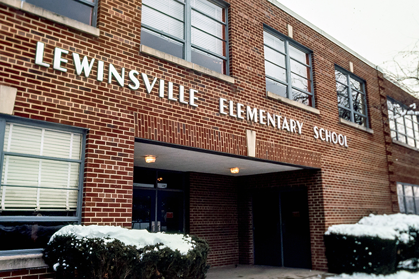 Color close-up photograph of the main entrance of Lewinsville Elementary School. There is snow on the bushes in front of the school.