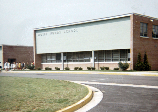 Color photograph of the front exterior of Mosby Woods Elementary School. Students are walking into the building.