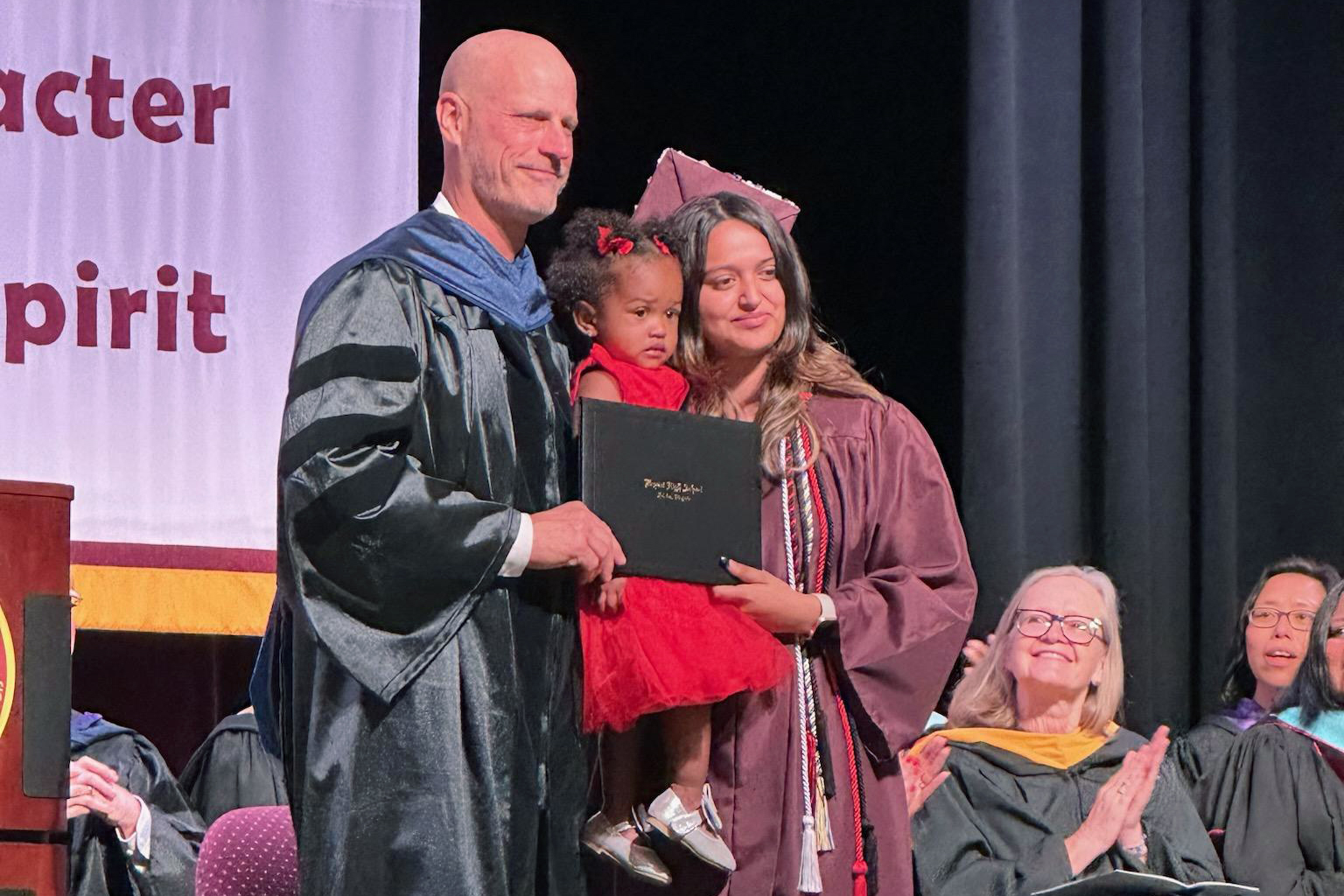 Newly-minted Bryant High School graduate Anyeli Salguero receives her diploma from principal Chris Larrick with her 20-month-old daughter in her arms.