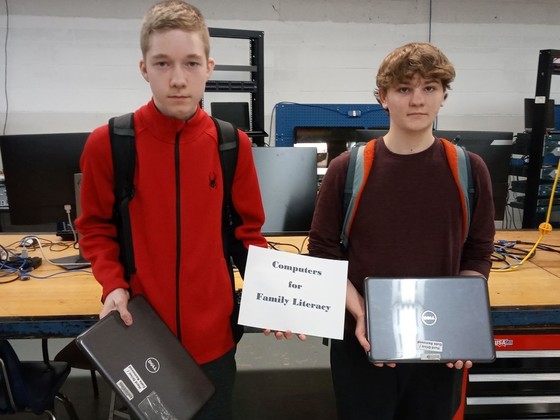 two students standing together holding laptops