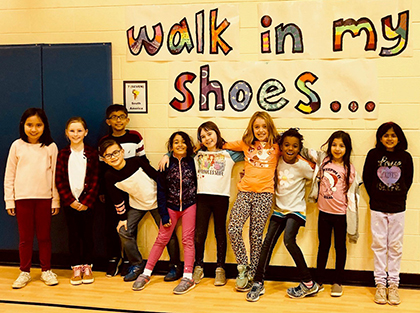 Students standing against a wall with a banner that reads "Walk in My Shoes"