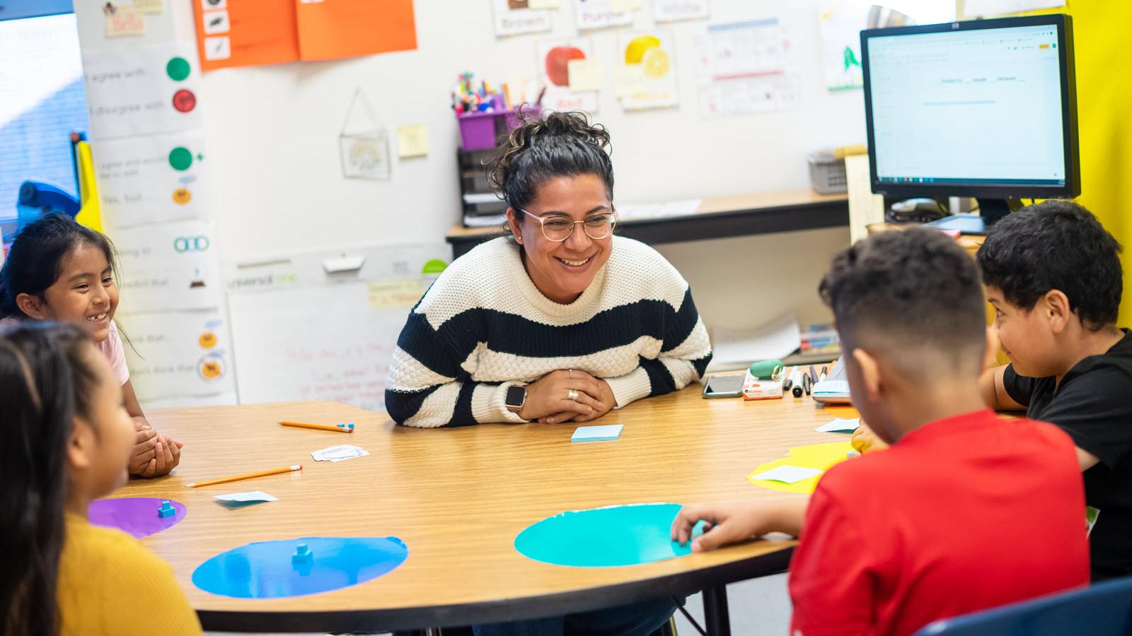 young teacher at table smiling at students